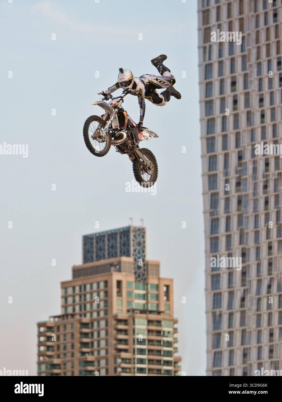 Pilota di motocross freestyle che esegue una acrobazia aerea ad alta quota sopra i grattacieli di una città moderna durante una mostra di sport estremi urbani. Foto Stock