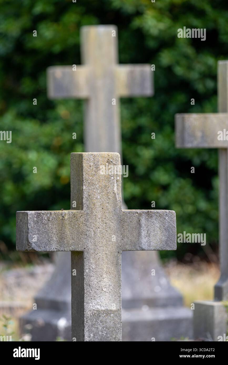 Pietre tombali incrociate in un cimitero, con l'attenzione su una e le altre fuori fuoco. Foto Stock