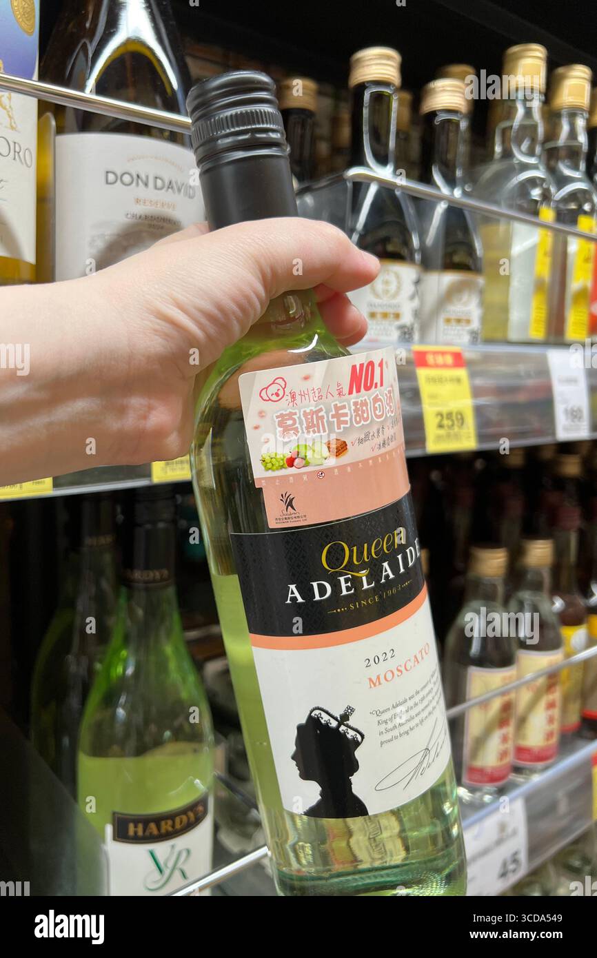 Una mano prende una bottiglia di vino bianco dallo scaffale di un supermercato Foto Stock
