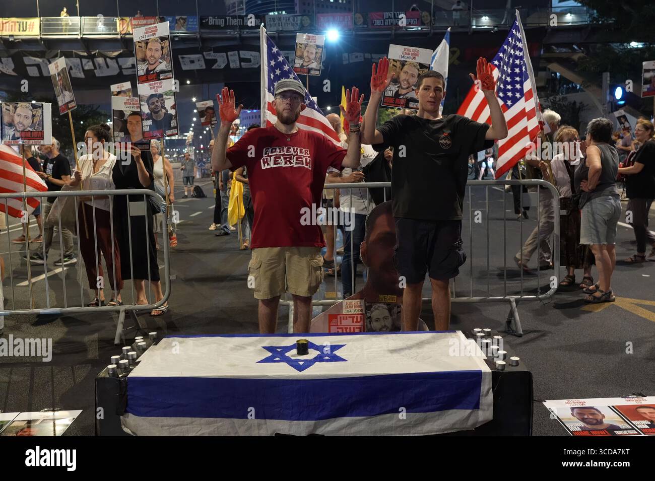 TEL AVIV, ISRAELE - 12 AGOSTO: I manifestanti alzano le mani dipinte di rosso per simboleggiare le vittime di guerra mentre si trovano dietro una bara allestita coperta da una bandiera israeliana per rappresentare gli ostaggi uccisi nella prigionia di Hamas durante una protesta fuori dal quartier generale dell'IDF che chiede la fine della guerra a Gaza e un'azione urgente per riportare in Israele gli ostaggi rimasti. Il 12 agosto 2025 a Tel Aviv, Israele. La manifestazione segue l'approvazione dei piani del primo ministro israeliano Benjamin Netanyahu di espandere l'occupazione dell'IDF della Striscia di Gaza per assumere il controllo completo della città di Gaza Foto Stock
