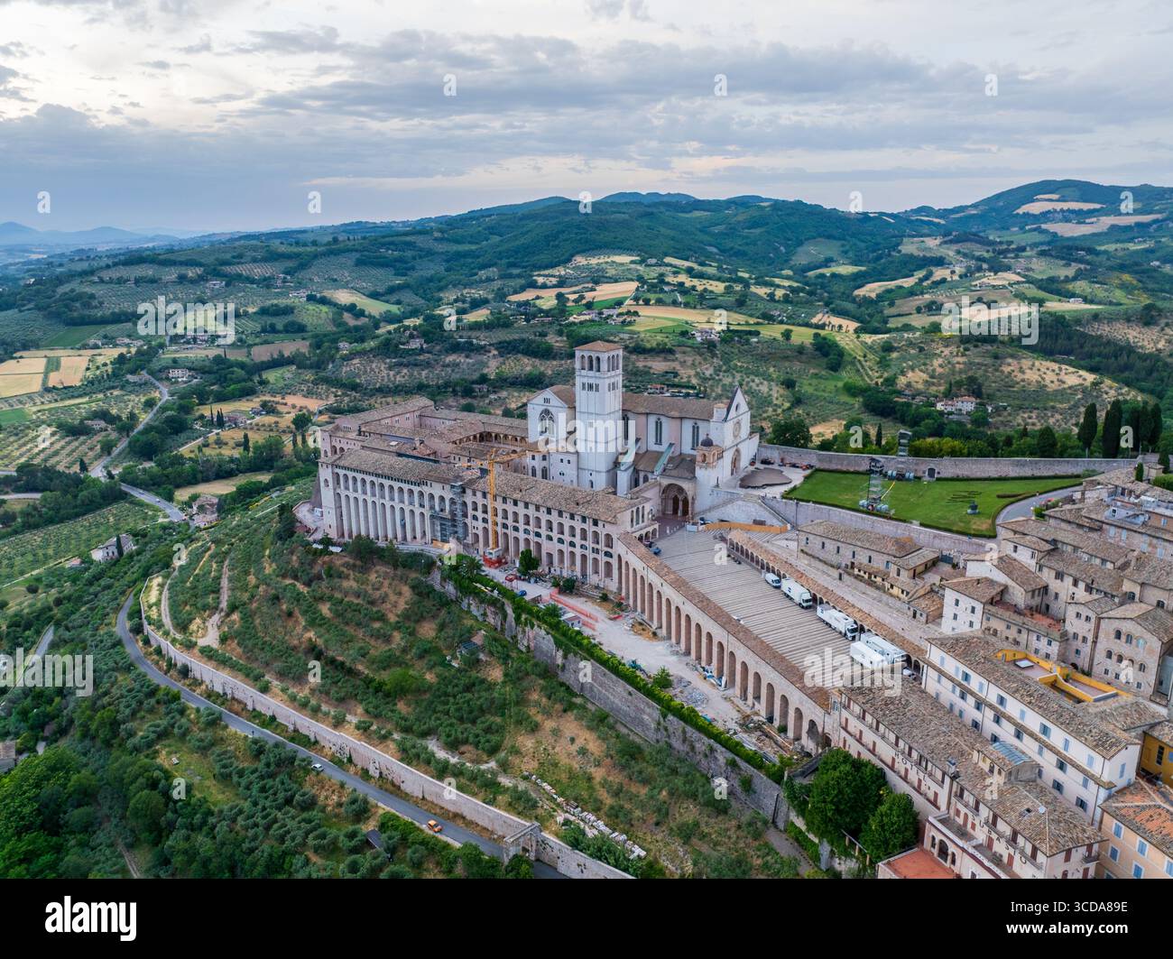 Veduta aerea della Basilica di San Francesco d'Assisi che si erge maestosamente sullo sfondo di dolci colline e campi verdeggianti, Perugia, Umbria, Italia. Foto Stock