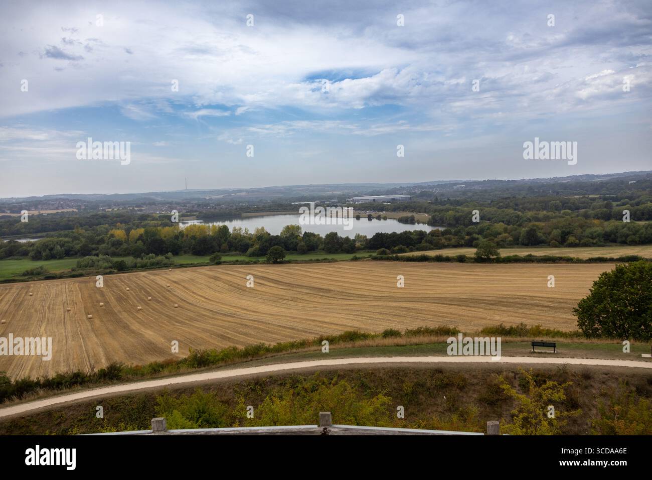 Vista panoramica di terreni agricoli, un sentiero tortuoso e un lago lontano sotto un cielo parzialmente nuvoloso Foto Stock
