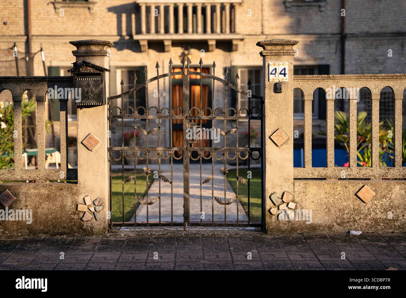 Cancello chiuso in ferro battuto con elementi decorativi, cassetta postale e targa del numero civico, che indica proprietà privata e sicurezza Foto Stock