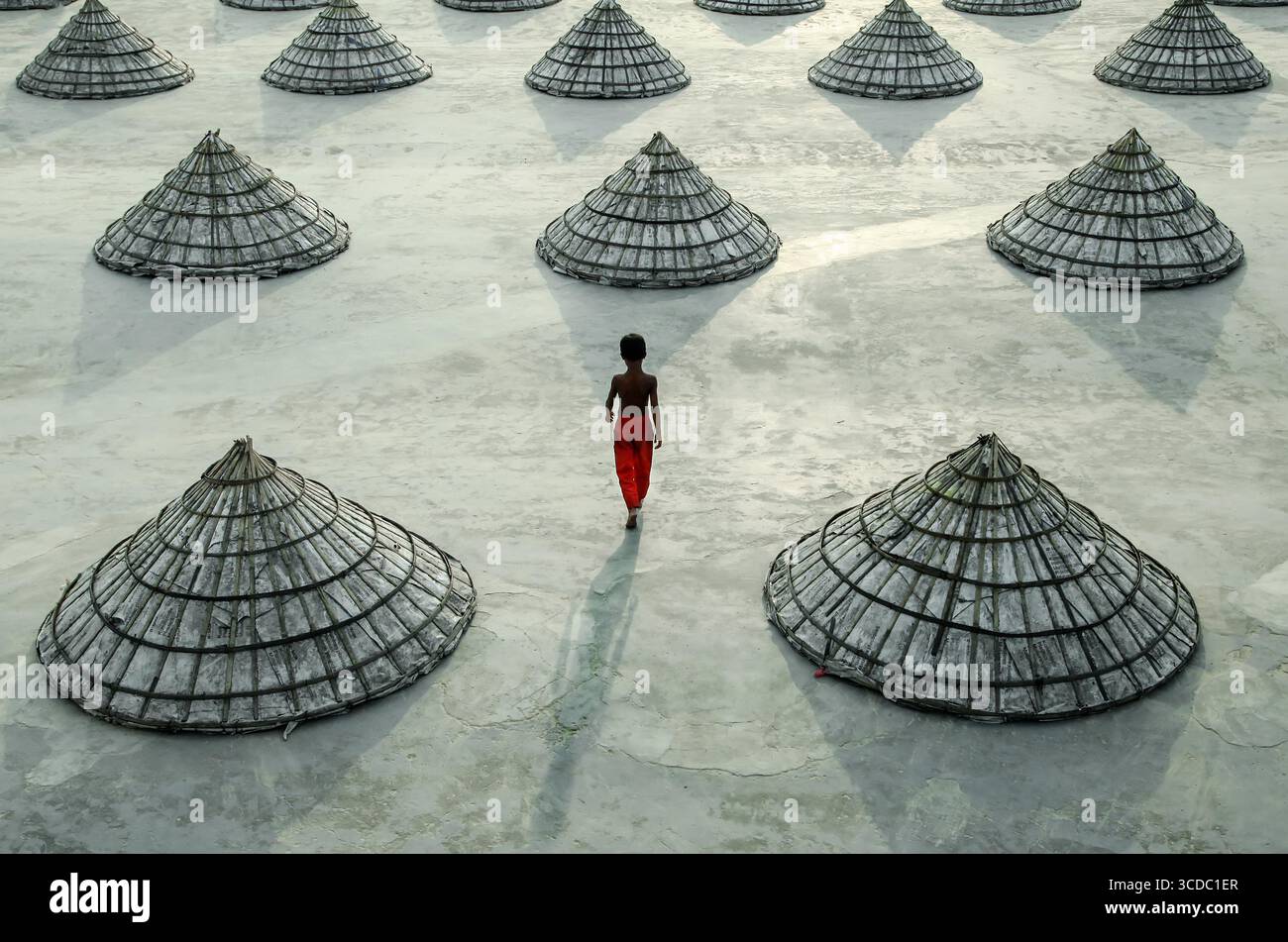 Brahmanbaria, Bangladesh - 8 giugno 2021: Veduta di una figura solitaria in rosso che cammina in mezzo a un mare di strutture coniche ordinate sotto il vasto cielo. Foto Stock