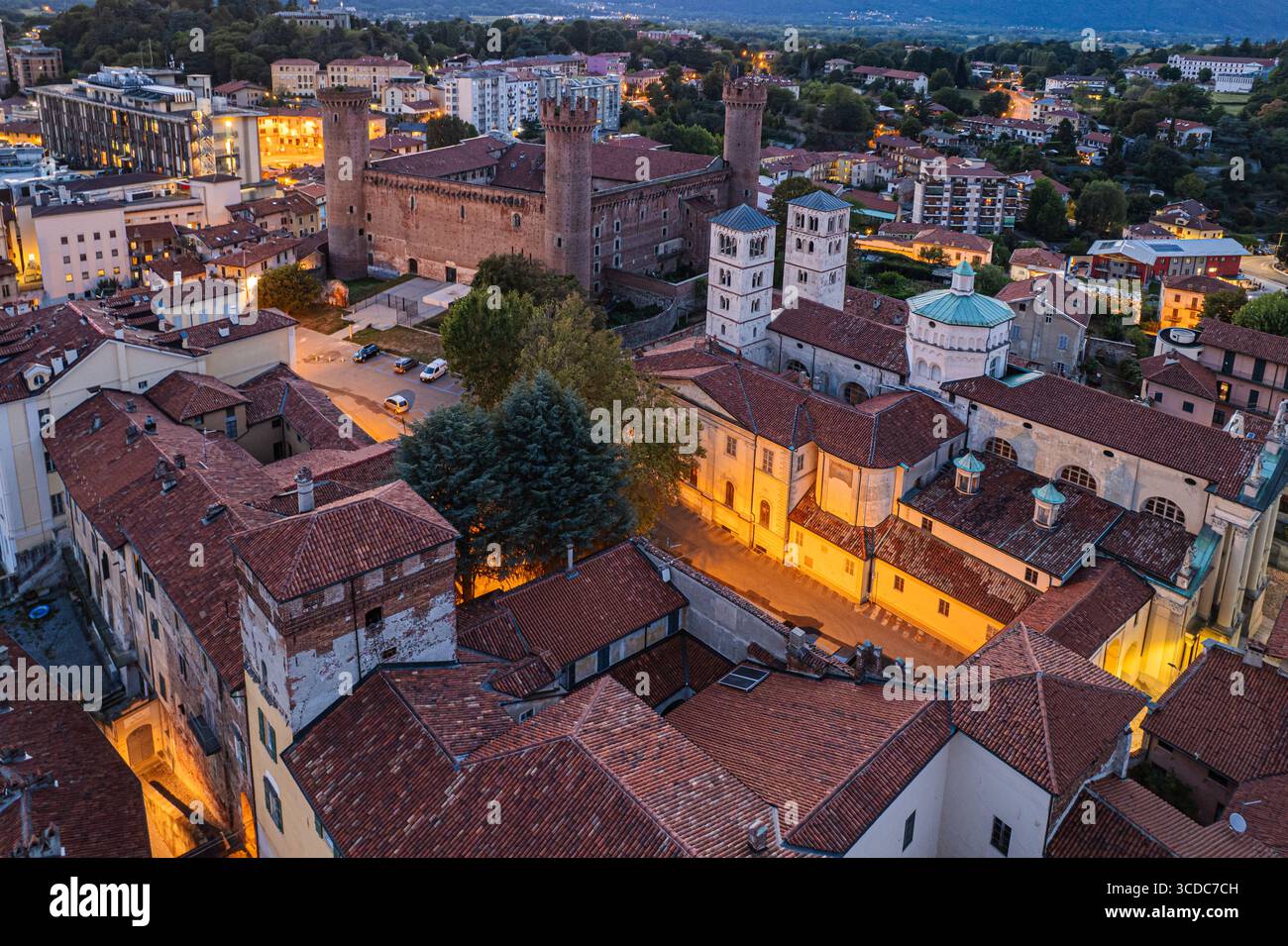 Vista aerea dei tetti di tegole rosse e delle antiche strutture di Ivrea, che mostrano il castello medievale e il Duomo, immersi nel caldo bagliore del crepuscolo, Ivrea, Piemonte, Italia. Foto Stock