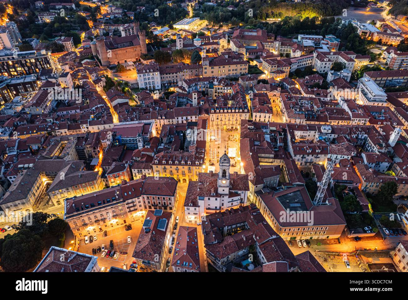Vista aerea della Piazza di città illuminata e degli edifici circostanti che emettono calde luci in mezzo alle fresche sfumature serali, Ivrea, Piemonte, Italia. Foto Stock