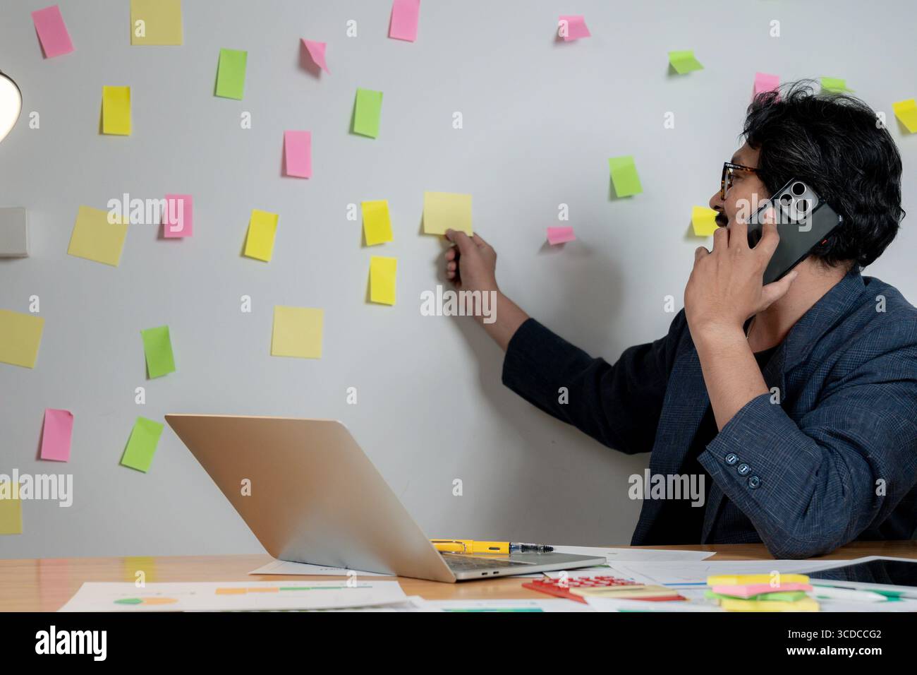 Un giovane uomo d'affari scrive idee su appunti e le attacca a un muro nel suo ufficio. Foto Stock