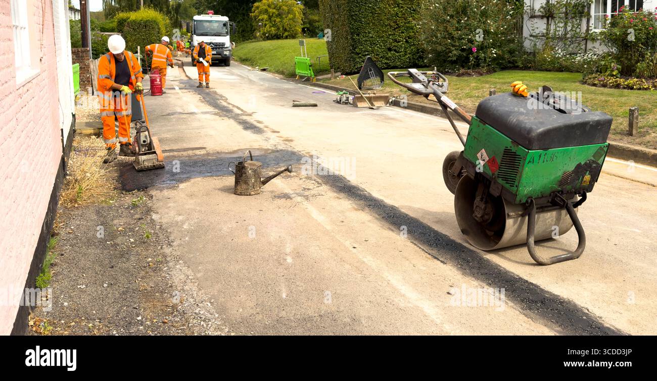 Winchester, Hampshire, Inghilterra, Regno Unito. 07.08.2025. Workman utilizza un compattatore per la posa dell'asfalto dopo l'installazione di una nuova rete interamente in fibra in una V Foto Stock
