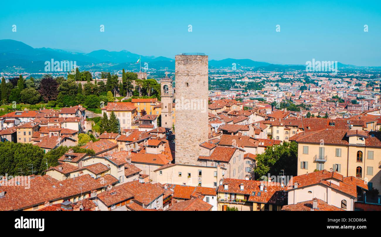 Torre del Gombito, un'alta torre medievale in pietra, sorge tra i tetti rossi della città alta di Bergamo, con la città e la montagna circostante Foto Stock