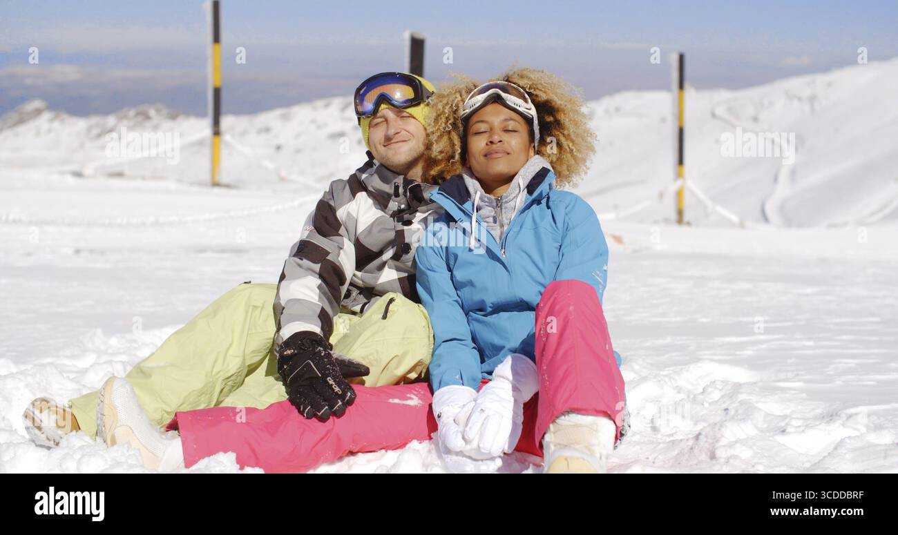 Giovane uomo e donna attraente in abiti da sci seduti sulla neve in montagna dopo una giornata intensa sulla pista Foto Stock