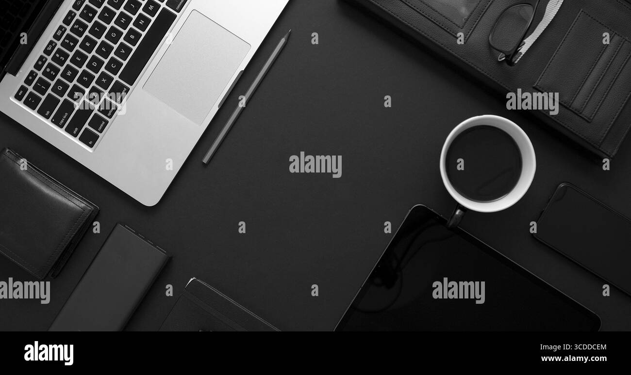 Concetto di desktop aziendale. Mix di materiali per ufficio e gadget su uno sfondo nero del tavolo. Con computer portatile, telefono cellulare, occhiali, notebook, tazza di caffè. Foto Stock