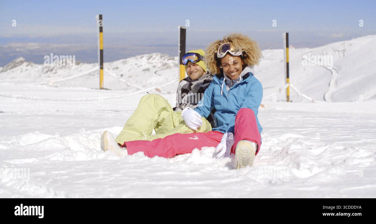 Giovane uomo e donna attraente in abiti da sci seduti sulla neve in montagna dopo una giornata intensa sulla pista Foto Stock