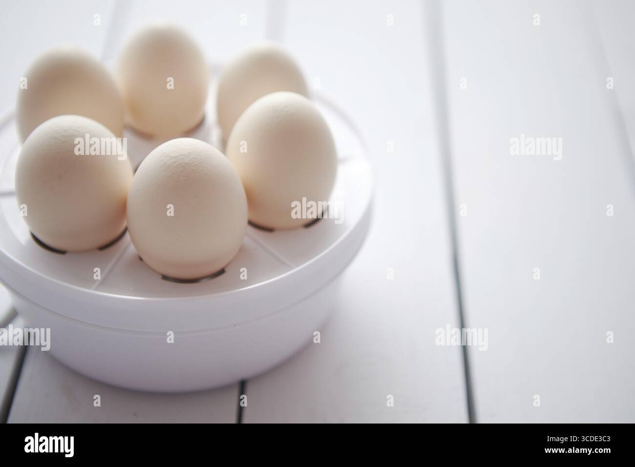 Uova di pollo in un fornello elettrico su un tavolo di legno bianco pronto per bollire Foto Stock