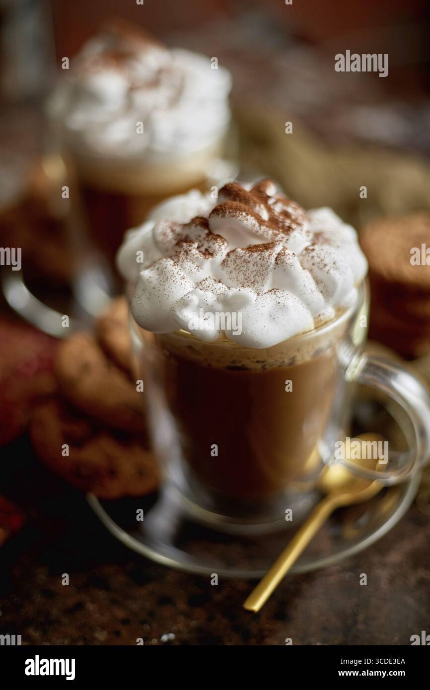 Due bicchieri alti con cioccolata calda, panna montata e cannella in polvere. Servito con biscotti al burro di cioccolato. Concetto di dolce dessert Foto Stock