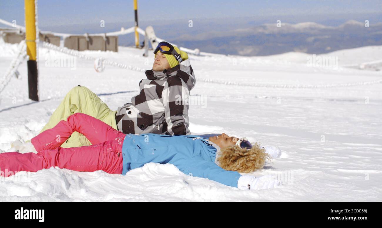 Giovane uomo e donna in abiti da sci che si rilassano per riposare sulla neve in montagna dopo una giornata intensa sulla pista Foto Stock
