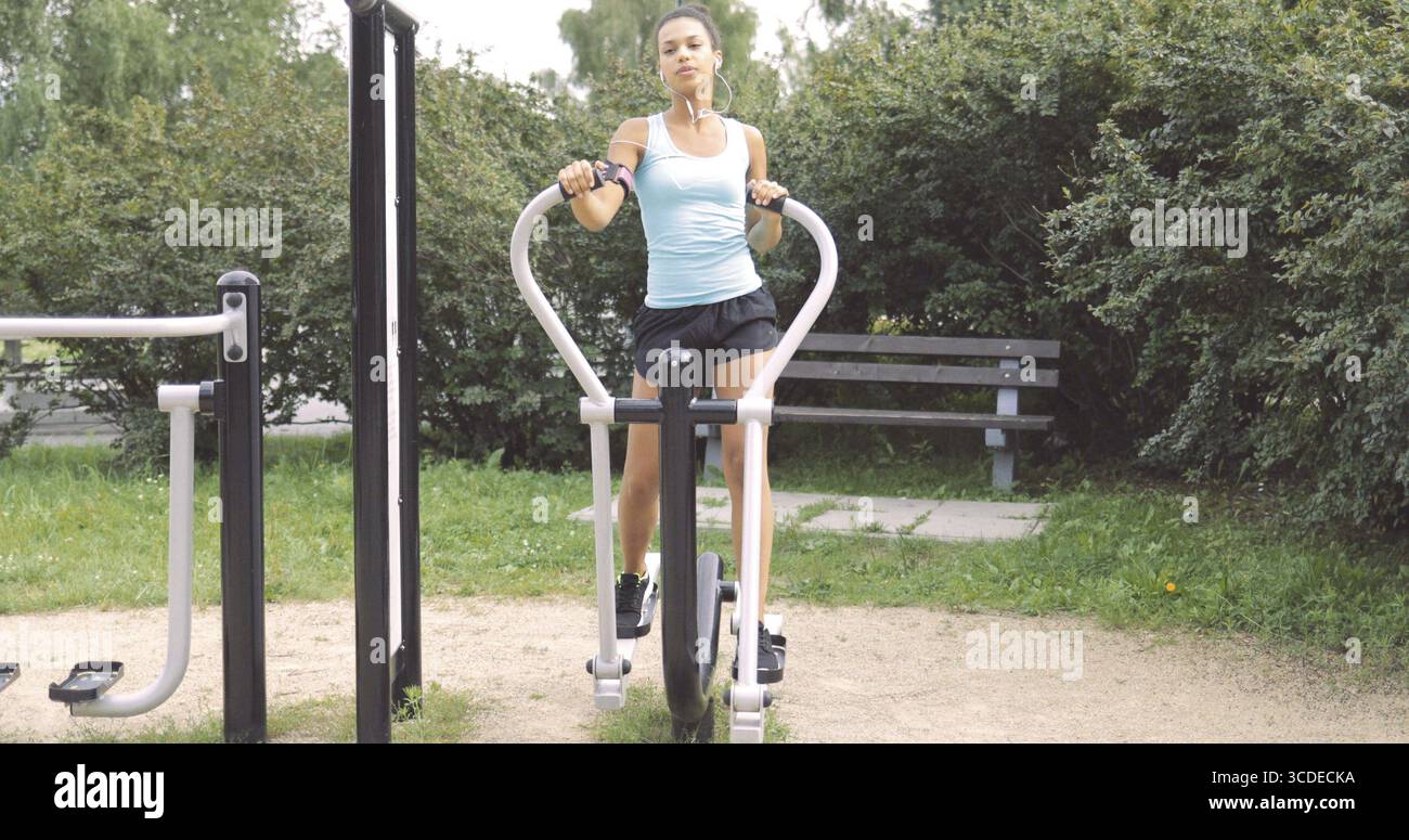 Giovane donna sicura di sé con abbigliamento sportivo che si allena con l'allenamento in palestra mentre ascolta la musica con lo smartphone e guarda lontano Foto Stock