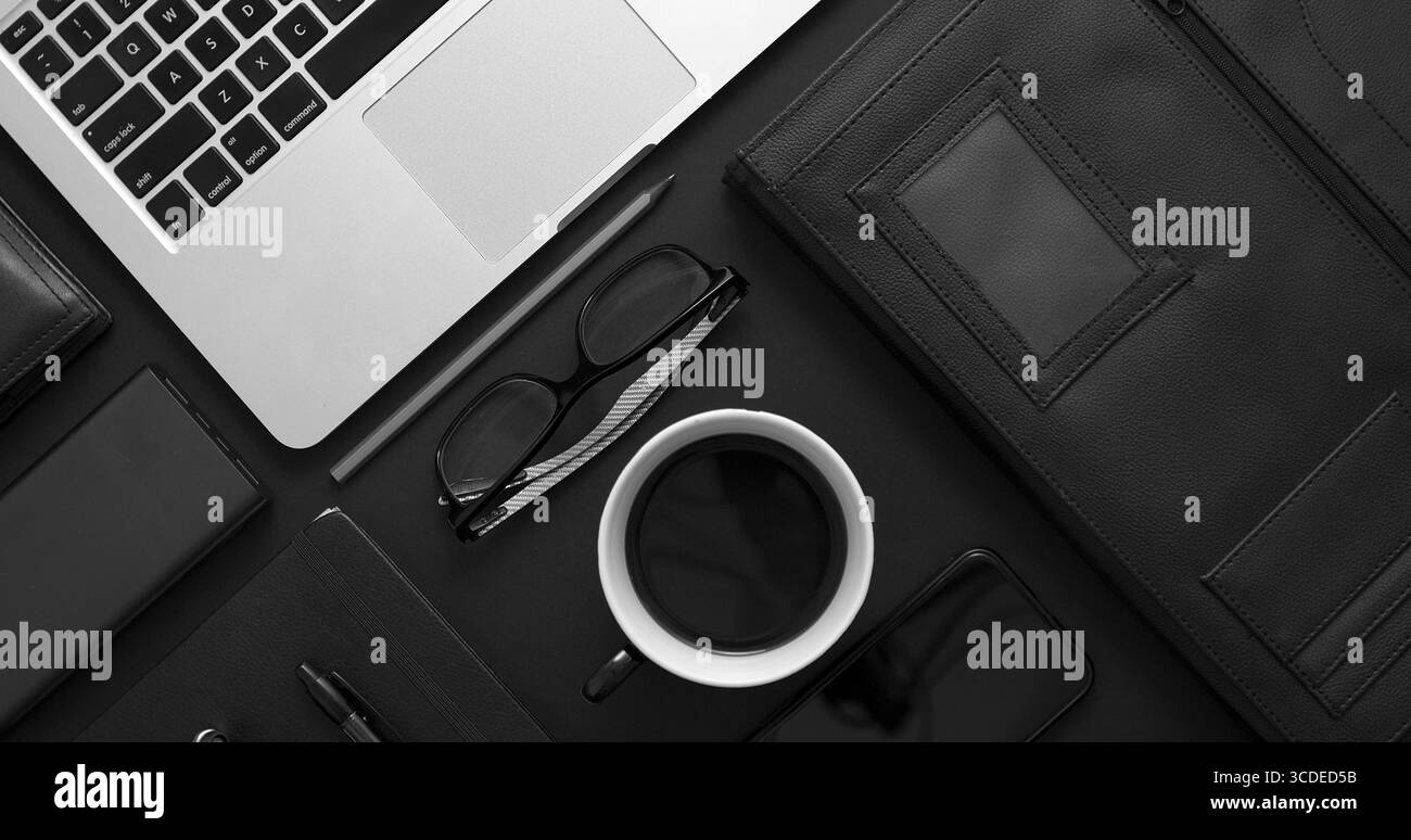 Concetto di desktop aziendale. Mix di materiali per ufficio e gadget su uno sfondo nero del tavolo. Con computer portatile, telefono cellulare, occhiali, notebook, tazza di caffè. Foto Stock