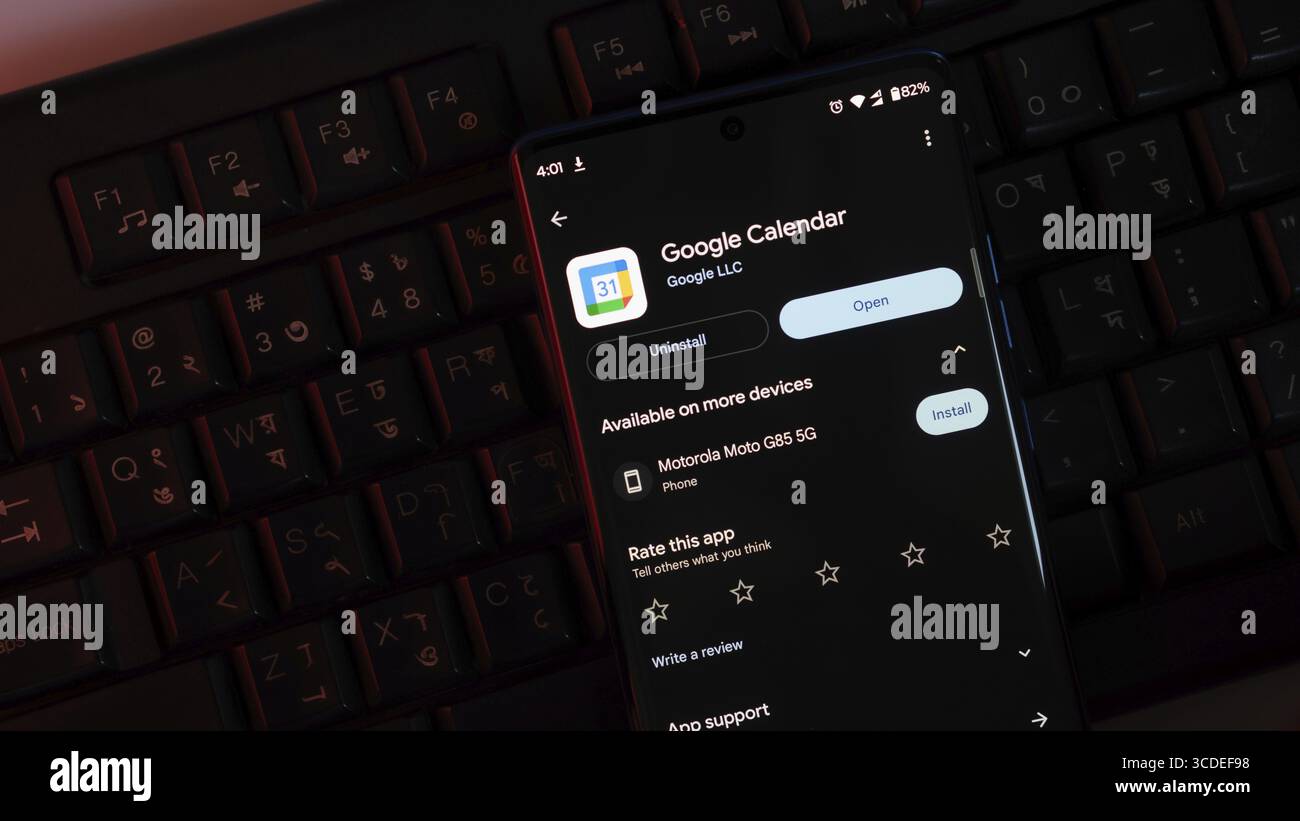 Un'app Google Calendar viene aperta sullo schermo di uno smartphone, posizionata su una tastiera in condizioni di scarsa illuminazione Foto Stock