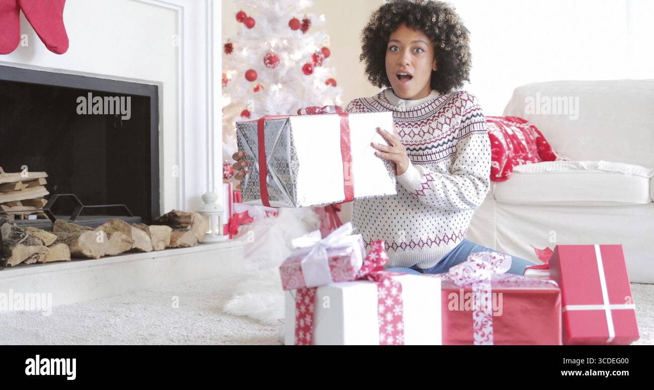 Sorpreso giovane donna tenendo un grande regalo di Natale nelle sue mani come si siede sul pavimento a casa sua apertura presenta Foto Stock