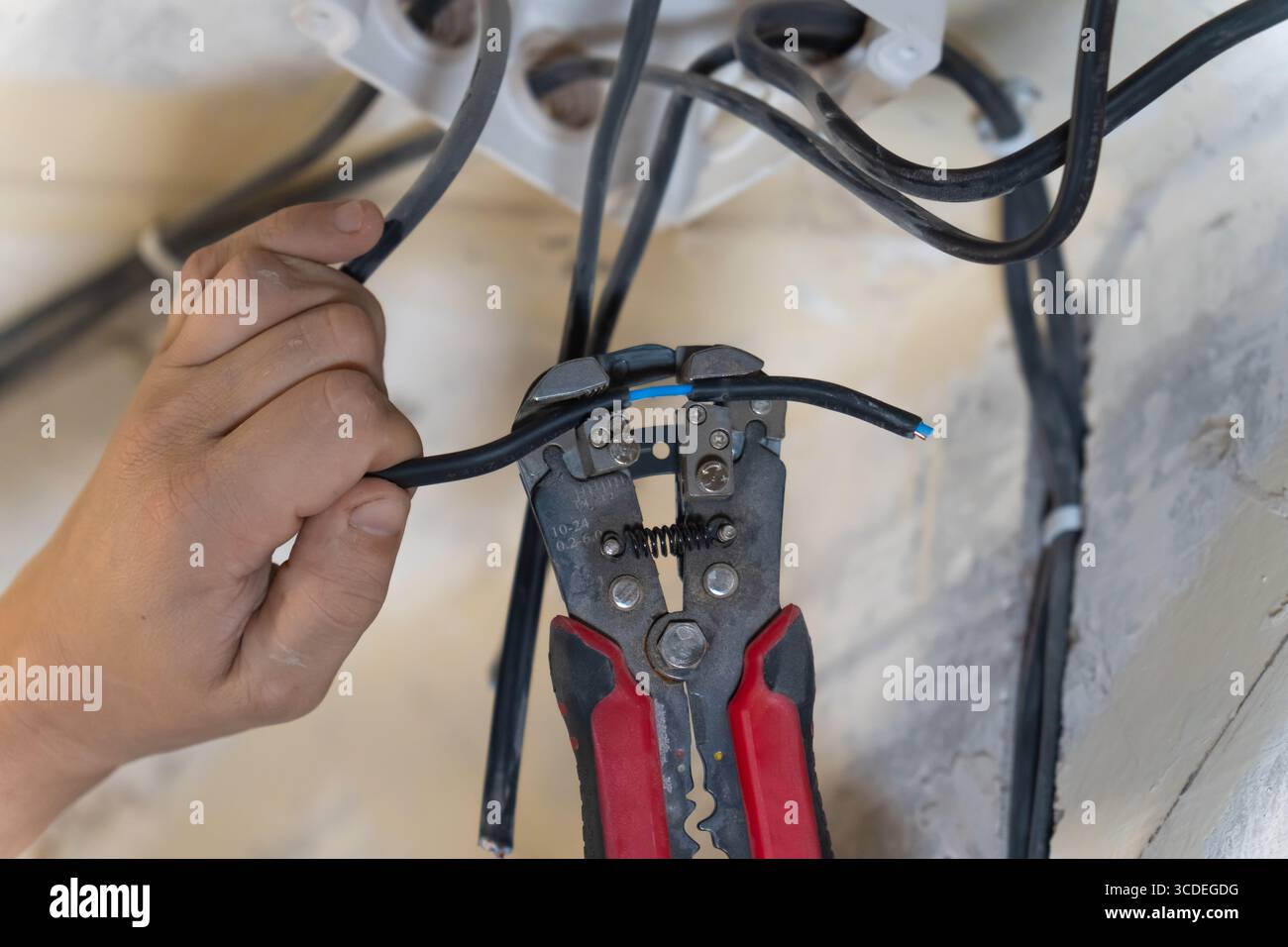 L'elettricista utilizza spelafili per rimuovere con cautela l'isolamento da un filo elettrico, preparandolo per il collegamento durante un'installazione elettrica Foto Stock