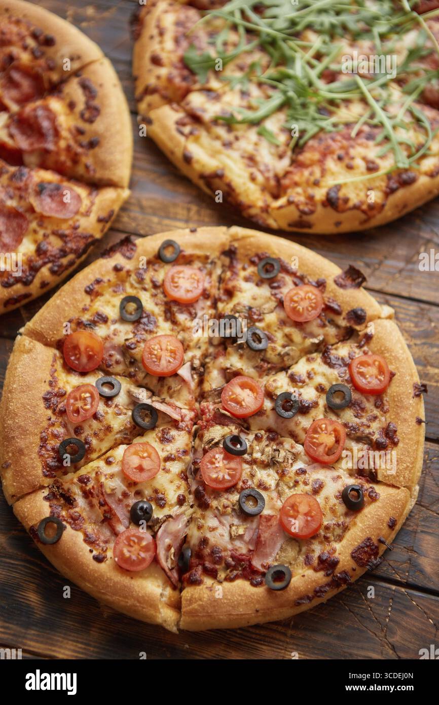 Composizione di tre tipi diversi di pizze poste su un tavolo di legno arrugginito e graffiato. Piatti caldi e freschi pronti da mangiare Foto Stock