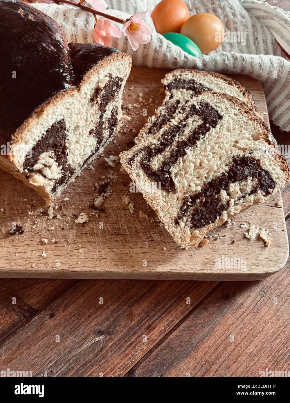 Cozonac, tradizionale dessert rumeno di pane dolce pasquale. Tagliare il pane dolce su un tagliere di legno e le uova di Pasqua sullo sfondo. Foto Stock