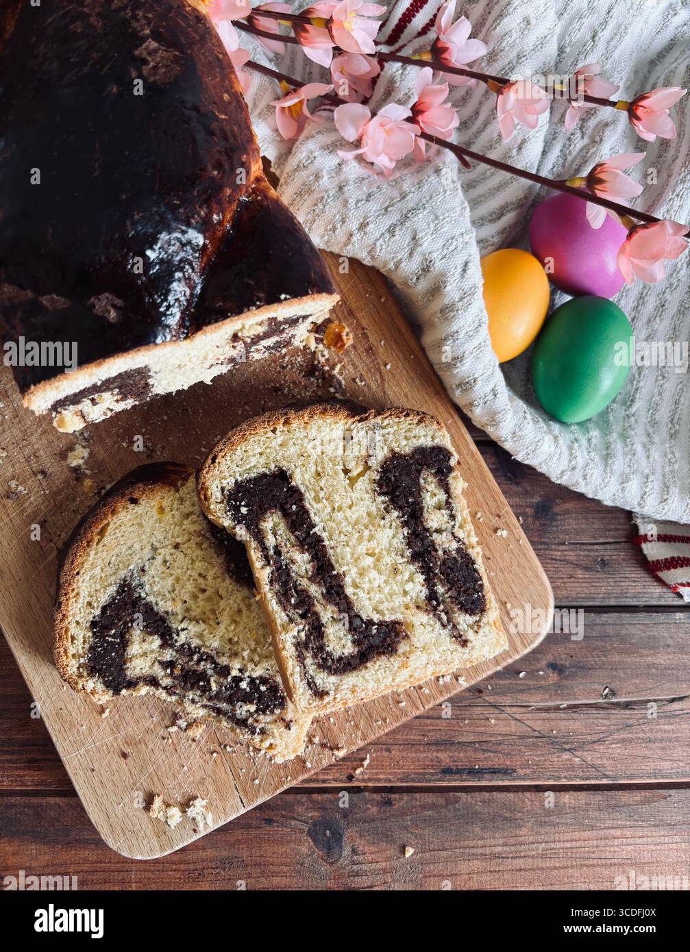 Cozonac, tradizionale dessert rumeno di pane dolce pasquale. Tagliare il pane dolce su un tagliere di legno e le uova di Pasqua sullo sfondo. Foto Stock