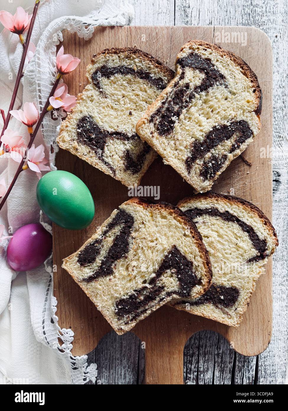 Cozonac, tradizionale dessert rumeno di pane dolce pasquale. Tagliare il pane dolce su un tagliere di legno e le uova di Pasqua sullo sfondo. Foto Stock