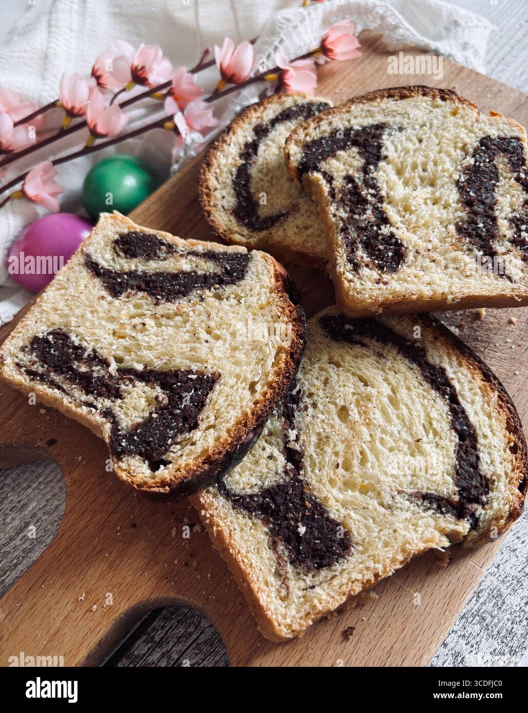 Cozonac, tradizionale dessert rumeno di pane dolce pasquale. Tagliare il pane dolce su un tagliere di legno e le uova di Pasqua sullo sfondo. Foto Stock