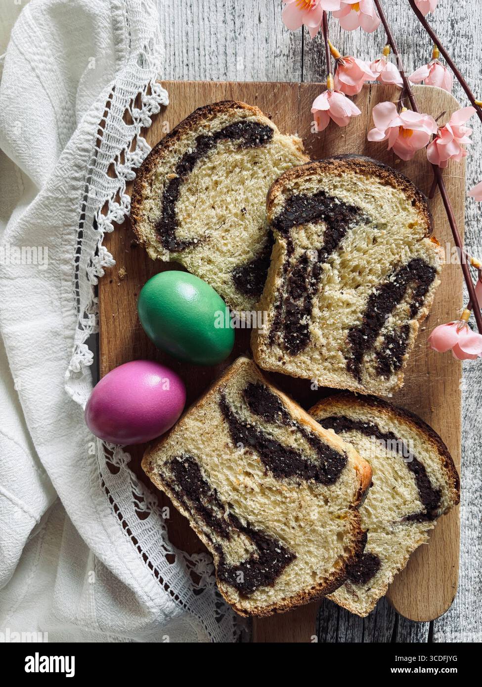 Cozonac, tradizionale dessert rumeno di pane dolce pasquale. Tagliare il pane dolce su un tagliere di legno e le uova di Pasqua sullo sfondo. Foto Stock