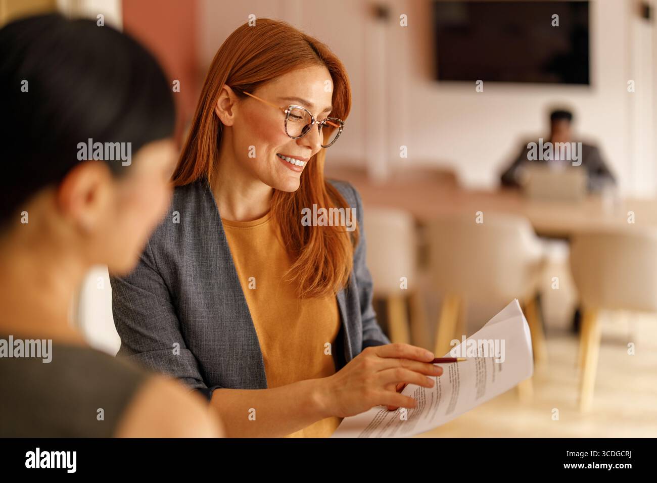 Avvocato donna sorridente in occhiali da vista che mostra documenti contrattuali a una donna d'affari mentre discute in ufficio Foto Stock