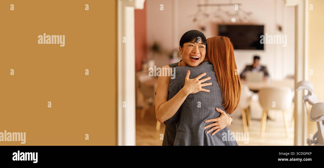 Una donna professionale positiva che abbraccia la collega e la accoglie in ufficio mostrando sostegno e incoraggiamento Foto Stock