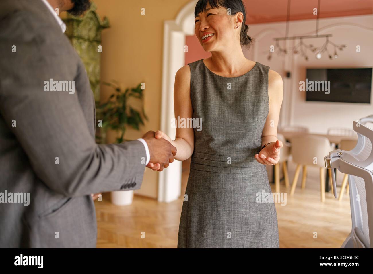Una donna felice che stringe la mano a un uomo d'affari dopo aver siglato un accordo durante la riunione d'ufficio Foto Stock