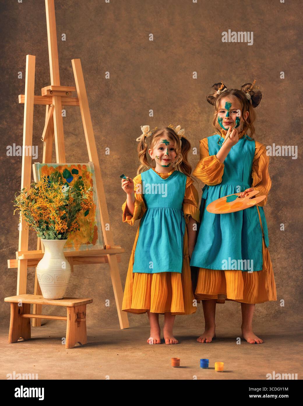 Due bambine e sorelle dipingono i fiori di mimosa su un cavalletto con delle pitture. Pittura, infanzia, felicità Foto Stock