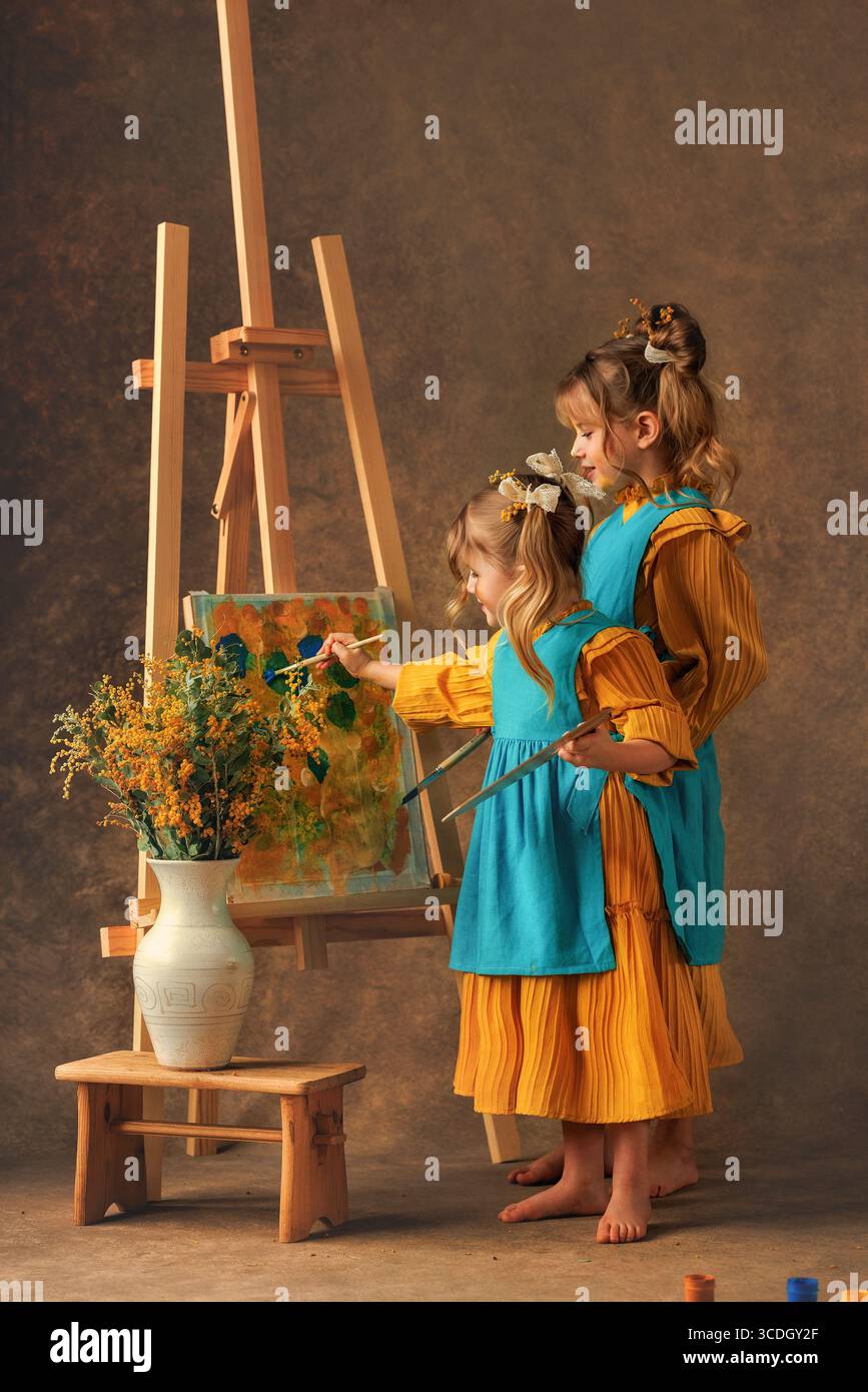 Due bambine e sorelle dipingono i fiori di mimosa su un cavalletto con delle pitture. Pittura, infanzia, felicità Foto Stock