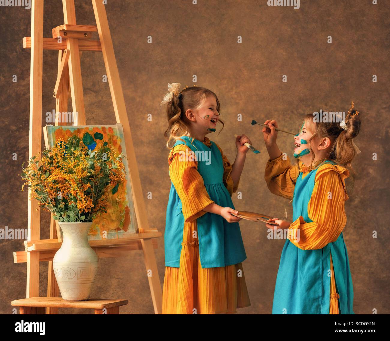 Due bambine e sorelle dipingono i fiori di mimosa su un cavalletto con delle pitture. Pittura, infanzia, felicità Foto Stock