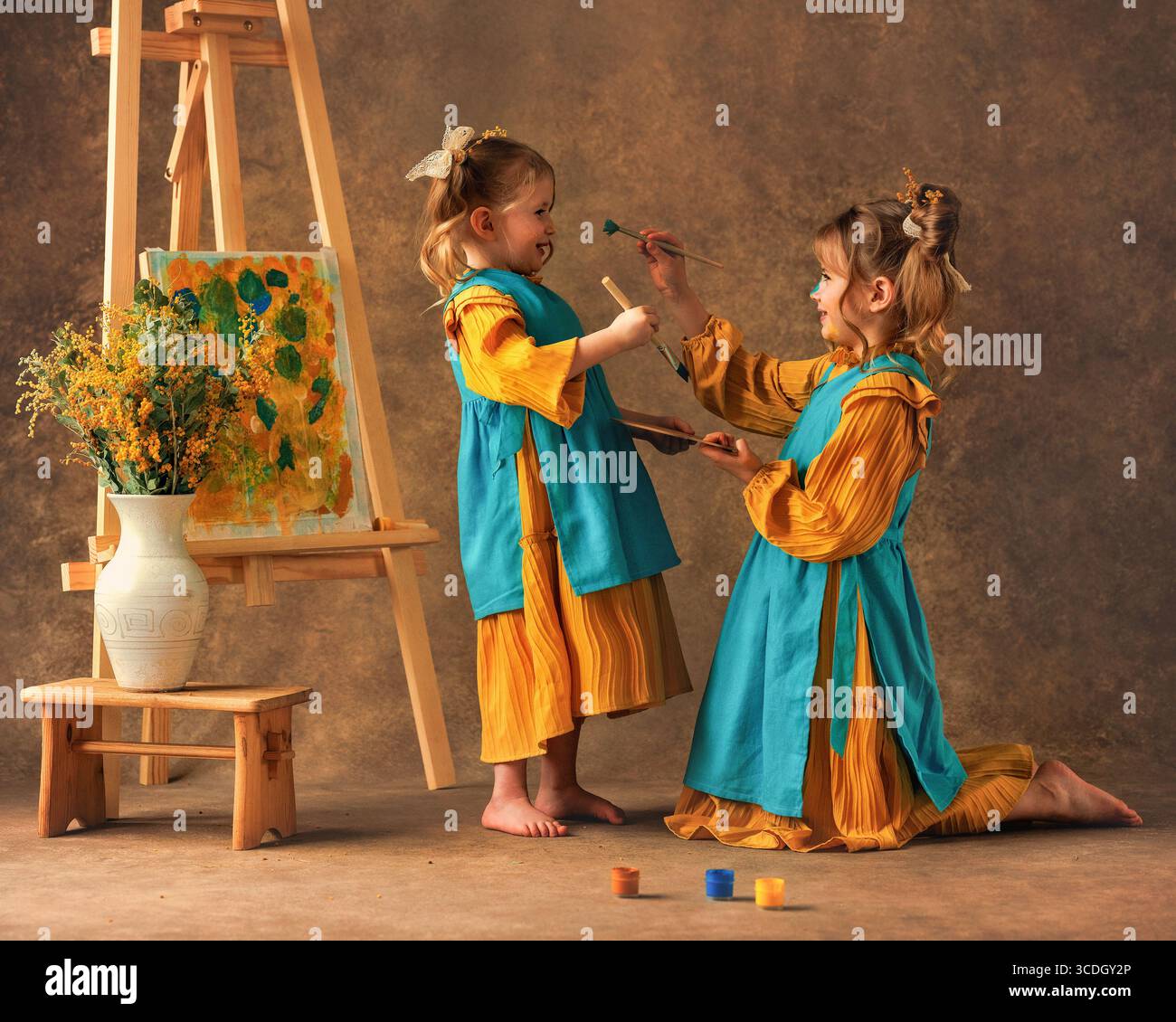 Due bambine e sorelle dipingono i fiori di mimosa su un cavalletto con delle pitture. Pittura, infanzia, felicità Foto Stock