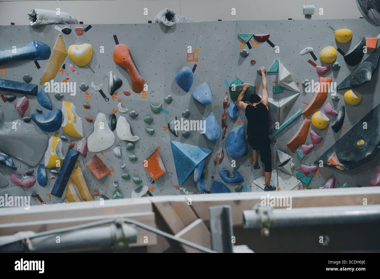 Boulderer è dotato di prese geometriche colorate su una parete interna, incorniciate da tubi esposti e condotti di ventilazione che aggiungono un tocco industriale alla palestra Foto Stock