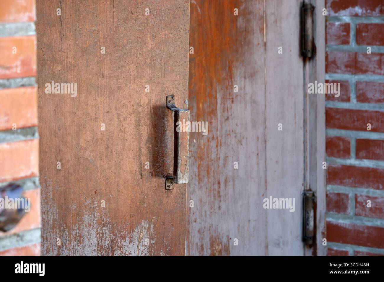 Una porta di legno intemprata è aperta contro un muro rustico di mattoni, che suscita curiosità. Foto Stock