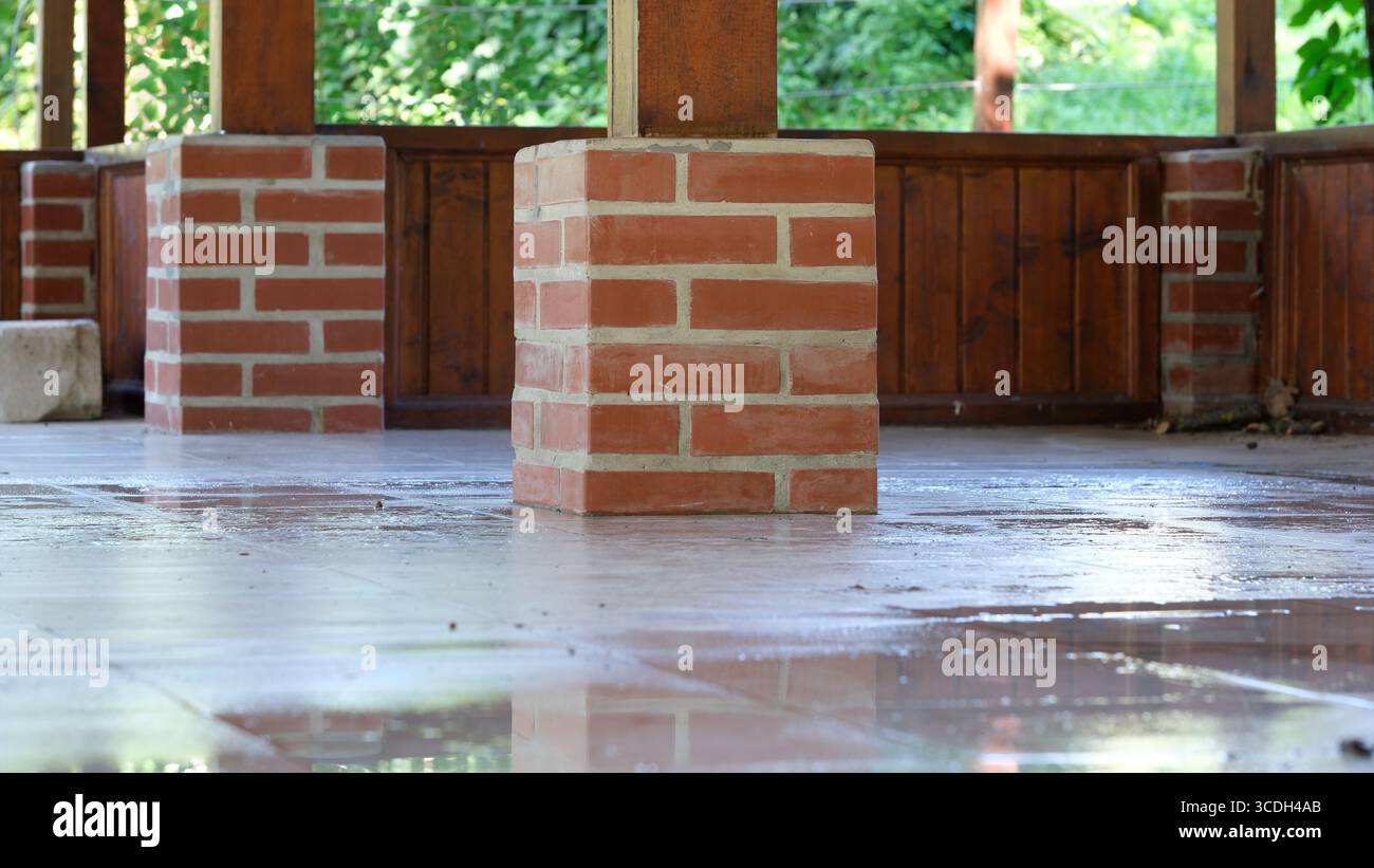 La luce del sole filtra tra gli alberi, mettendo in risalto una colonna di mattoni in uno spazio all'aperto sereno. Foto Stock