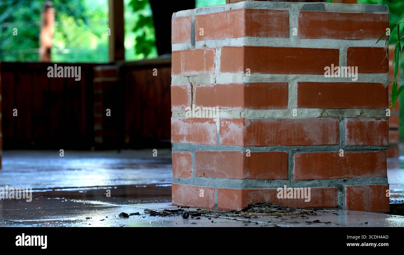 Il sole scorre attraverso gli alberi, illuminando una colonna di mattoni in un tranquillo cortile. Foto Stock