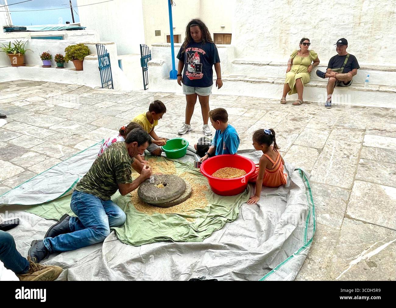 Il mais viene macinato con una smerigliatrice per pietra in un quadrato ad Amorgos. Il mais sarà utilizzato per preparare il pane al Panagia il 15 agosto. Foto Stock