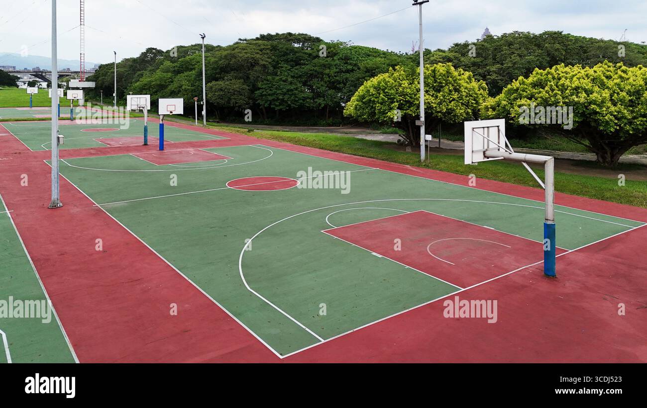 Un campo da pallacanestro vuoto all'aperto con più cerchi e campi dipinti di rosso e verde vicino alla cintura degli alberi Foto Stock