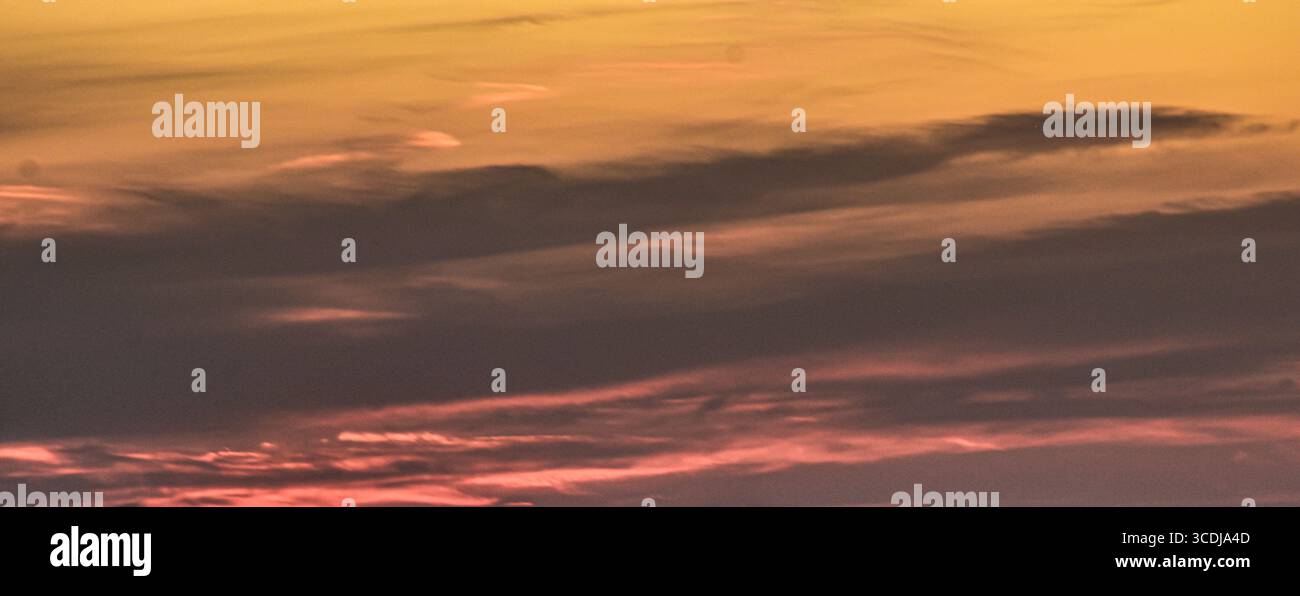 Cielo tranquillo e colorato al tramonto con nuvole sparse in tonalità calde e brillanti, perfetto per i temi della natura. Foto Stock