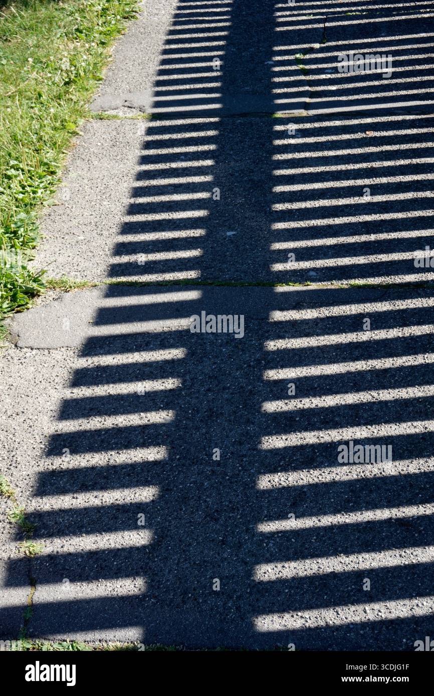 Ombra di recinzione in legno gettata sul marciapiede Foto Stock