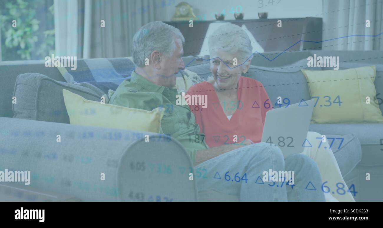 Una coppia senior che esamina i dati delle scorte su un notebook color argento nel soggiorno, con cuscini gialli Foto Stock