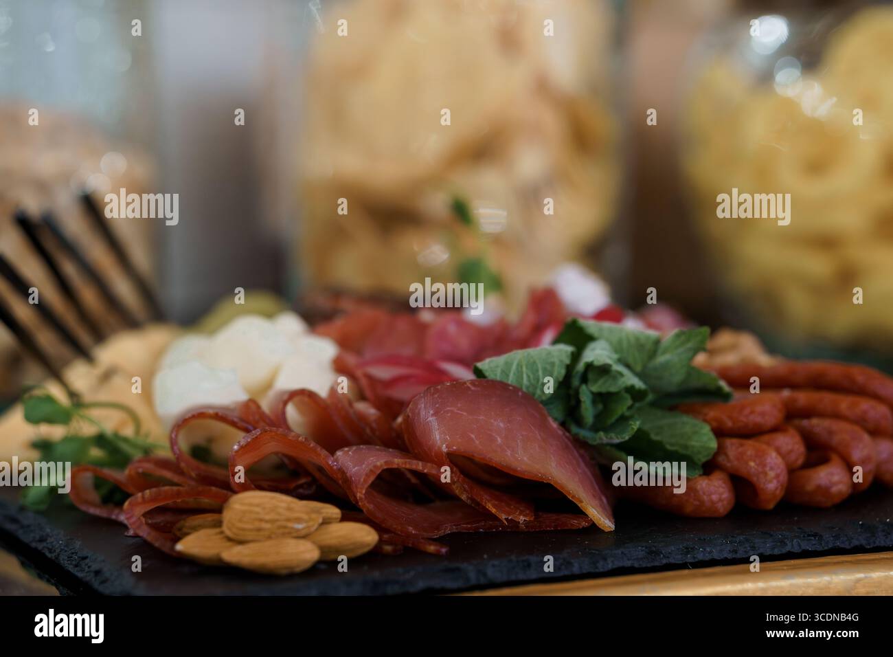 Una vista ravvicinata mostra un tagliere di salumi elegantemente organizzato con prosciutto, salame, vari formaggi, mandorle ed erbe fresche, adatto per Foto Stock