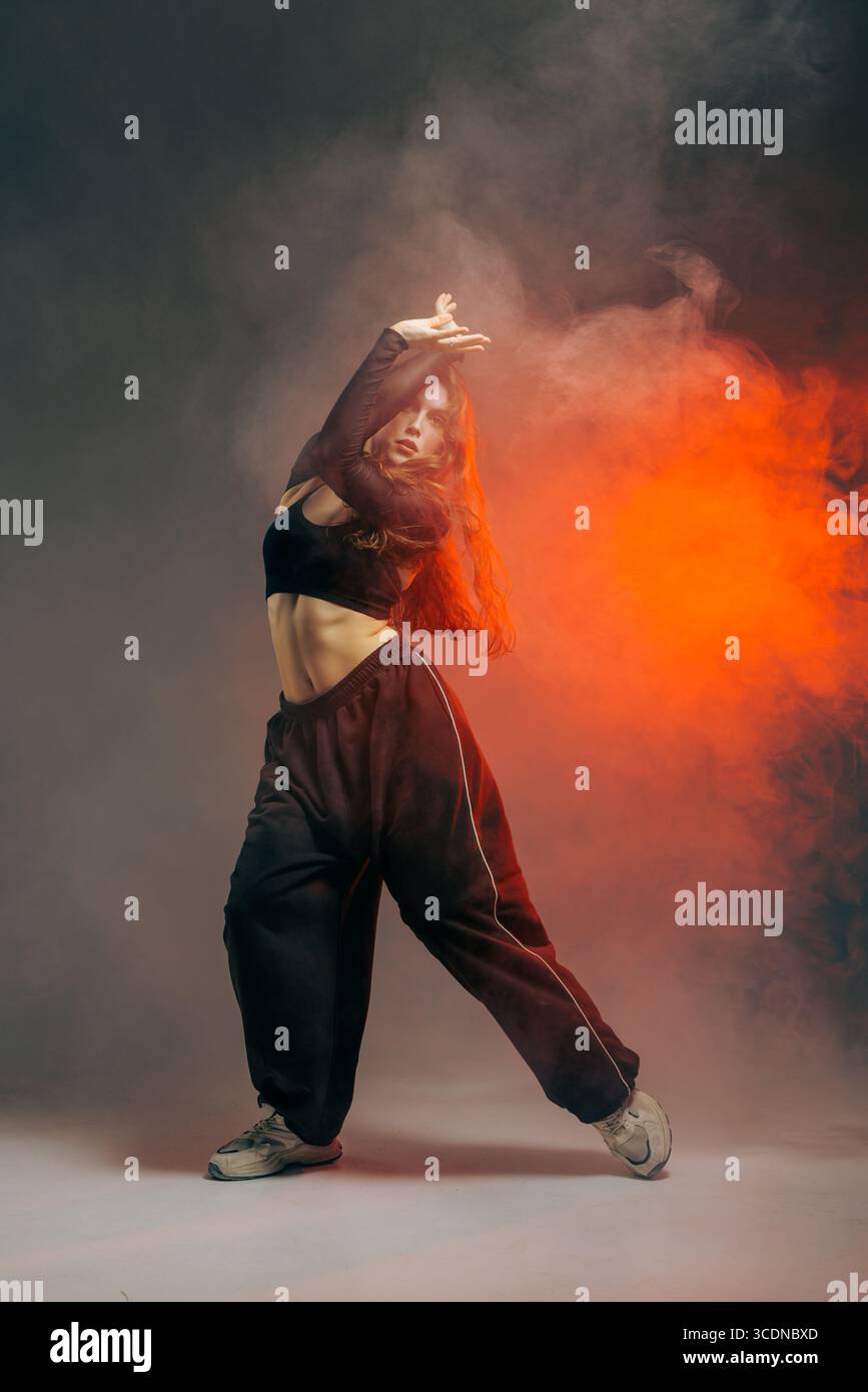 Ballerina jazz funk con pantaloni in stile urbano, che si distingue per una posa dinamica con movimento espressivo ed effetti di fumo creativi. Foto Stock