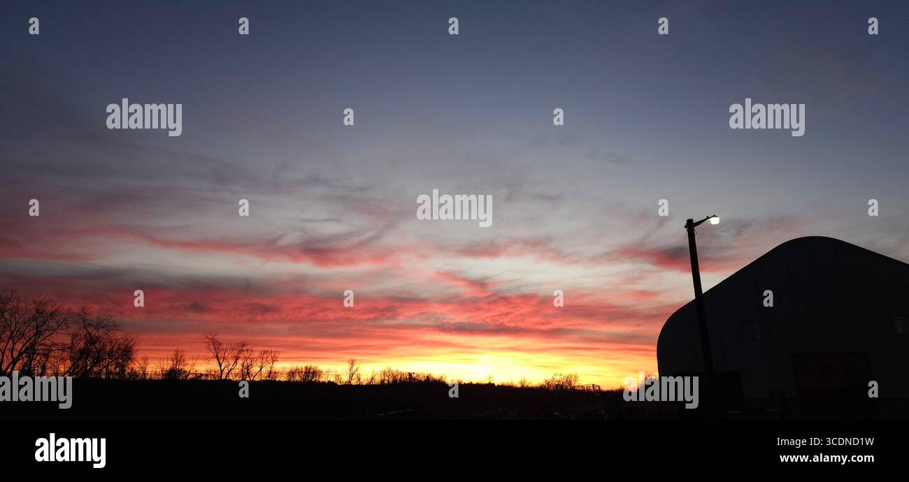 Splendido tramonto con alberi e un edificio. Le nuvole riflettono perfettamente il sole che tramonta mostrando la sua bellezza. - Immagine stock catturata con smartphone