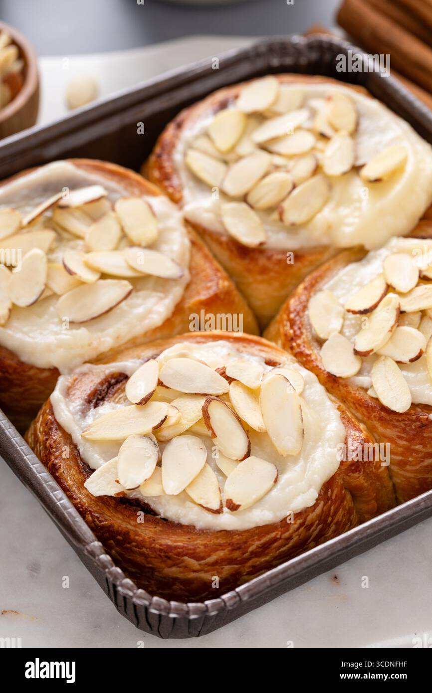 Involtini alla cannella ricoperti di glassa di formaggio spalmabile e mandorle affettate, appena sfornati e pronti da mangiare Foto Stock
